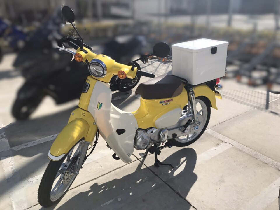 白のHondaラゲージボックスを取り付けた黄色のスーパーカブ